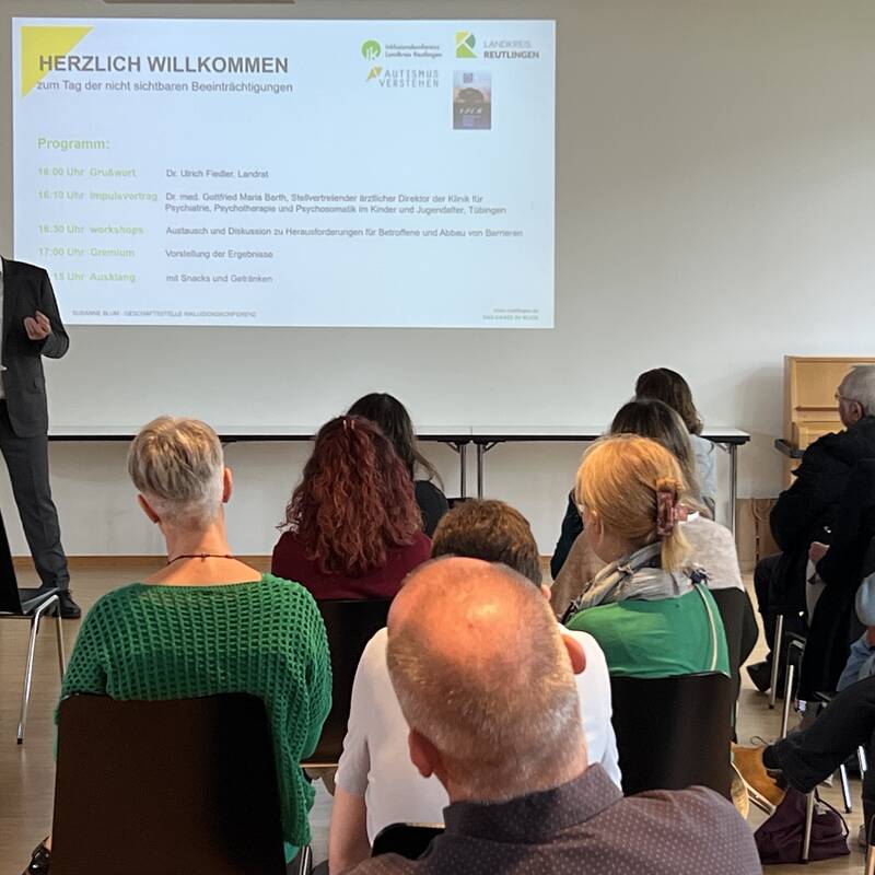 Landrat Dr. Fiedler begrüßt Gäste, während eine Präsentation mit dem Titel "HERZLICH WILLKOMMEN" im Hintergrund auf der Leinwand angezeigt wird.