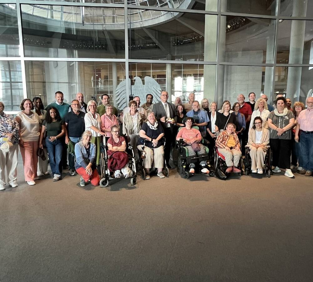 Eine Gruppe von Menschen, darunter einige im Rollstuhl, posiert für ein Foto vor der Botschaft vom Land Baden-Württemberg.