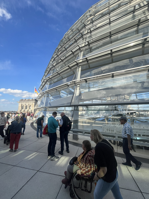 Eine Gruppe von Menschen befindet sich auf der Dachterrasse der Reichstagskuppel in Berlin bei sonnigem Wetter.