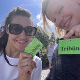 Zwei lächelnde Frauen halten grüne Schilder mit der Aufschrift „Tribüne“ in die Kamera.