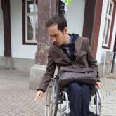 Ein Rollstuhlfahrer zeigt mit dem Finger auf Kopfsteinpflaster