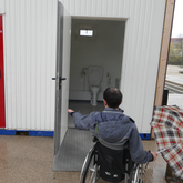 Ein Mann im Rollstuhl vor der Rampe in einen barrierefreien Toilettencontainer