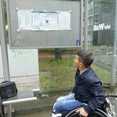 Eine Rollstuhlfahrerin versucht einen zu hoch hängenden Fahrplan zu lesen
