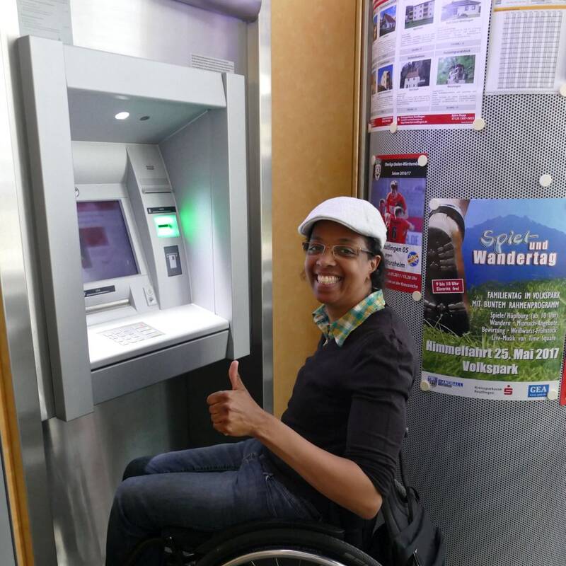Eine Rollstuhlfahrerin am Bankautomat mit Daumen hoch