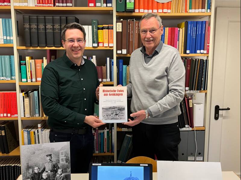 Zwei Männer stehen in einer Bibliothek vor einem Tisch mit einem Laptop und historischen Fotos, und halten ein Buch mit dem Titel "Historische Fotos aus Geislingen" hoch.