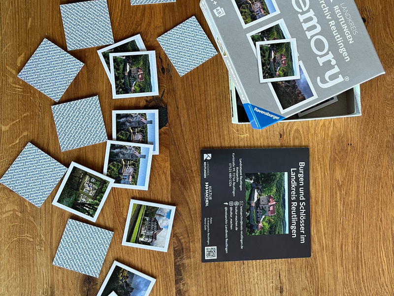 Eine Memory-Spielbox mit Karten, die Burgen und Schlösser im Landkreis Reutlingen zeigen, liegt geöffnet auf einem Holztisch ausgebreitet.