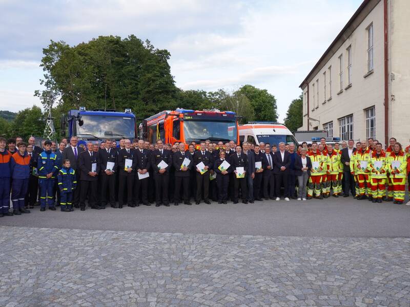 Eine große Gruppe von Menschen in Uniformen steht vor mehreren Einsatzfahrzeugen und einem Gebäude für ein Gruppenfoto.