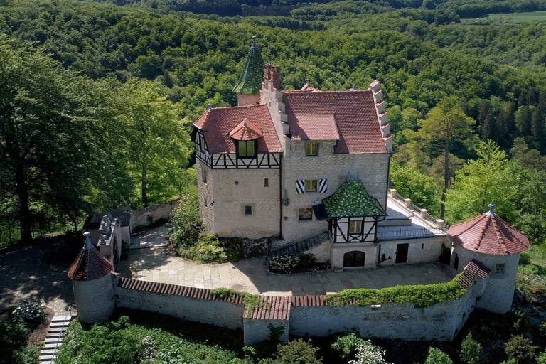 In Mitten von Hügeln und Wäldern eine kleine Burg mit einem ummauerten Burghof.