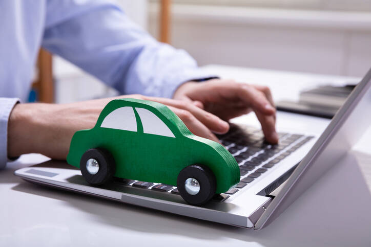 Auf einem Laptop liegt ein grünes Spielzeugauto, während jemand darauf tippt.