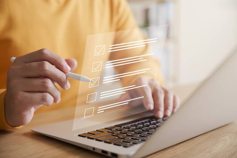 Eine Person benutzt einen Stift, um eine digitale Checkliste auf einem Laptop zu markieren.