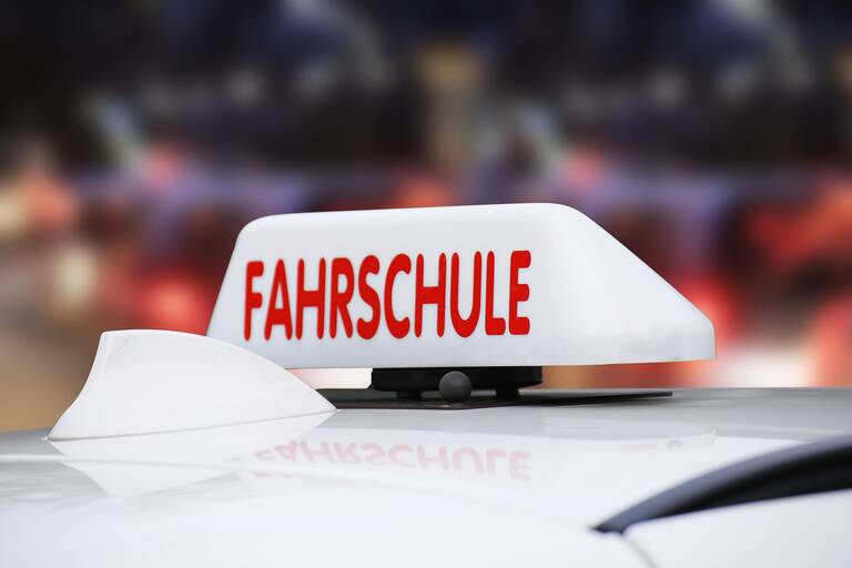 Ein weißes Schild mit der roten Aufschrift "Fahrschule" ist auf dem Dach eines Fahrzeugs montiert.