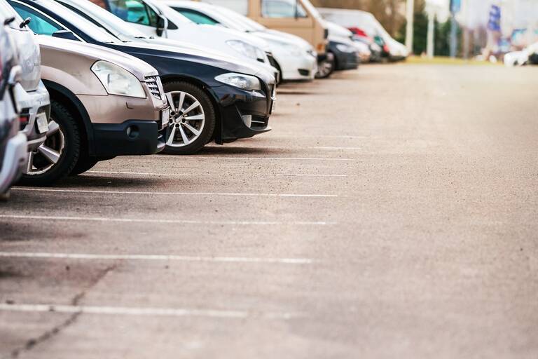 Bilck auf grauen Parkplatz mit einer Reihe parkender Autos am linken Bildrand