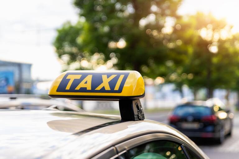 Dach eines gelben Taxis mit Taxischild im Vordergrund parkt an einem Straßenrand