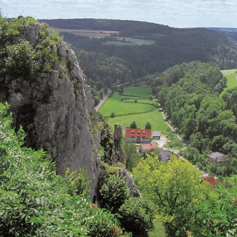 Ein kleines Schlösschen in einem Tal. Rund herum sind Hügel.