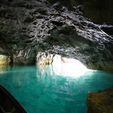 Das Bild zeigt eine Höhle mit leuchtend blauem Wasser und einem strahlend hellen Eingang, der die Felsen beleuchtet.