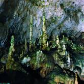 Eine Höhle mit mehreren grünen und braunen Stalagmiten und Stalaktiten, die von der Decke und dem Boden ragen.