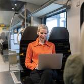 Eine Frau mit kurzen Haaren und einem Laptop auf dem Schoss sitzt in einem Vierer-Abteil in einem Zug.