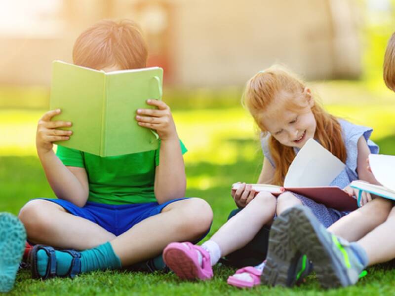 Vier Kinder sitzen auf einer Wiese und lesen aufmerksam in ihren Büchern.