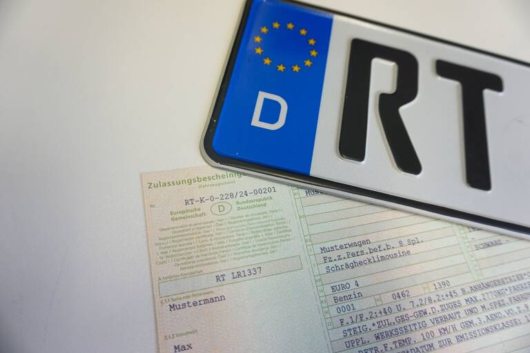 Ein Teil eines Kennzeichens auf einem weißen Tisch. Man sieht die Aufschrift RT. Darunter liegt eine hellgrüne Zulassungsbescheinigung.