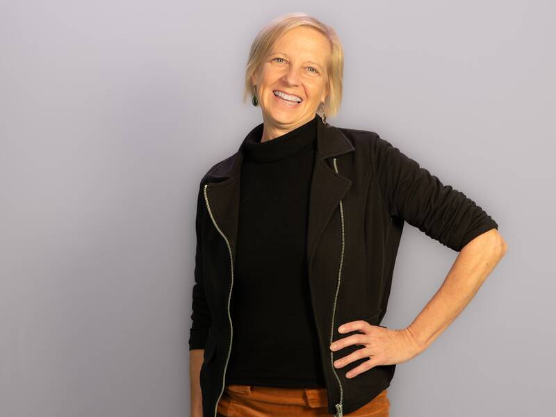 Portrait einer Frau mit blonden Haaren. Sie lächelt und trägt eine schwarze Jacke.