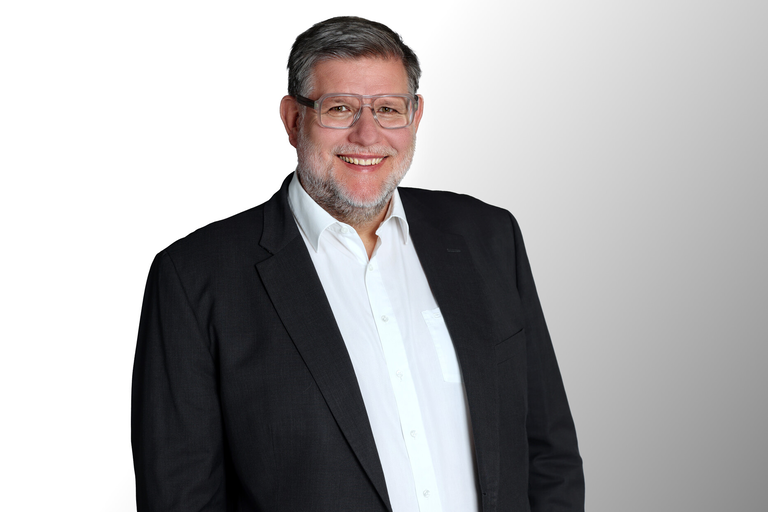 Ein Mann mittleren Alters in einem schwarzen Anzug und Brille.