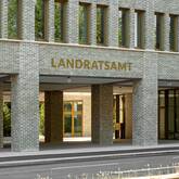 Das Bild zeigt die Fassade eines modernen Gebäudes mit der Aufschrift "LANDRATSAMT", bestehend aus hellen Backsteinen und vielen Fenstern.