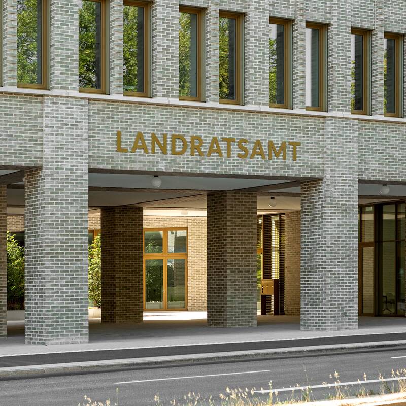 Das Bild zeigt die Fassade eines modernen Gebäudes mit der Aufschrift "LANDRATSAMT", bestehend aus hellen Backsteinen und vielen Fenstern.