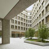 Ein moderner Innenhof eines Gebäudes mit großen Fenstern und zwei bepflanzten Beeten in der Mitte.