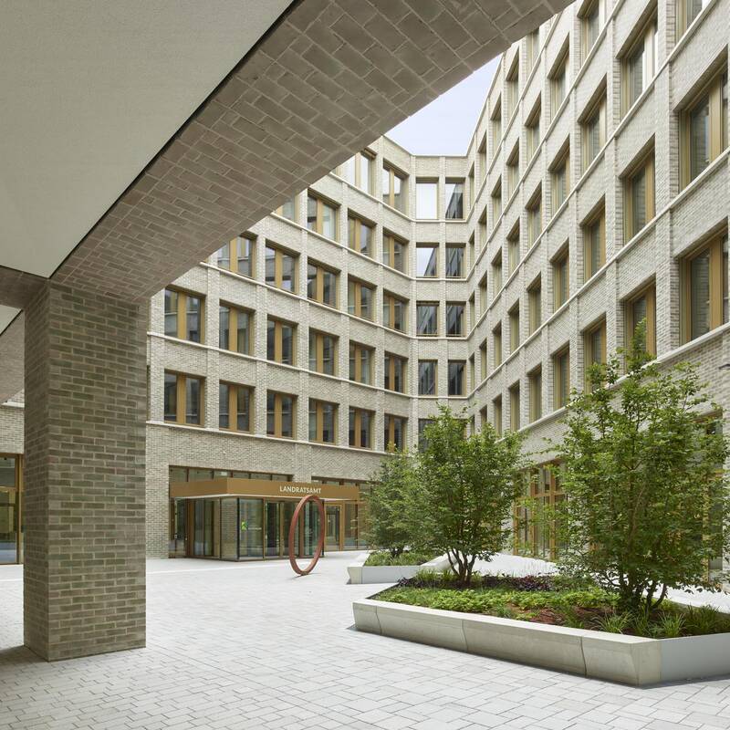 Ein moderner Innenhof eines Gebäudes mit großen Fenstern und zwei bepflanzten Beeten in der Mitte.