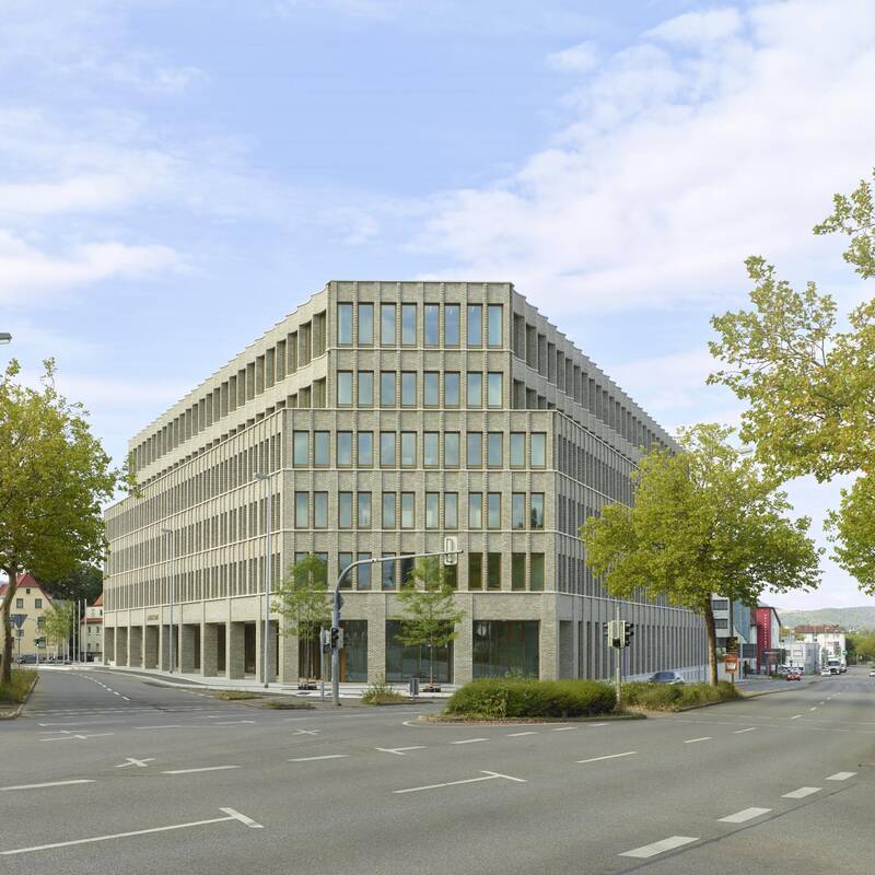 Ein modernes, eckiges Bürogebäude aus Beton und Glas steht an einer Straßenecke, umgeben von Bäumen und Straßenlaternen.