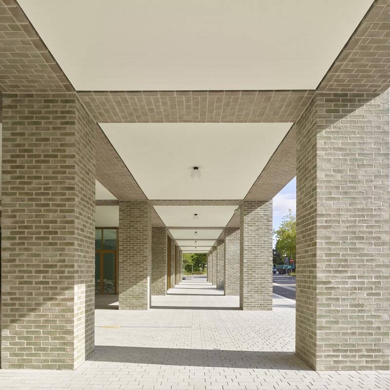 Ein überdachter Gehweg mit großen Ziegelpfeilern erstreckt sich entlang einer Straße, die von Bäumen gesäumt ist.