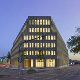 Ein modernes, fünfstöckiges Bürogebäude mit beleuchteten Fenstern steht an einer Straßenkreuzung in der Dämmerung.