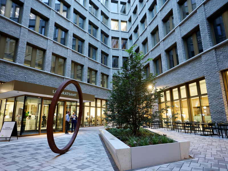 Ein Innenhof mit einem modernen Gebäudekomplex, einem großen Baum in der Mitte und einem Eingangsbereich mit der Aufschrift "Landratsamt".