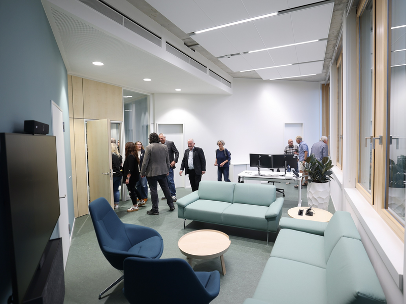 Der Raum ist modern eingerichtet mit Sofas und Sesseln und wird von mehreren Menschen besucht.