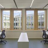 Ein modernes Büro mit zwei Arbeitsplätzen, Schreibtischen und Stühlen, das große Fenster mit Blick auf das angrenzende Gebäude hat.
